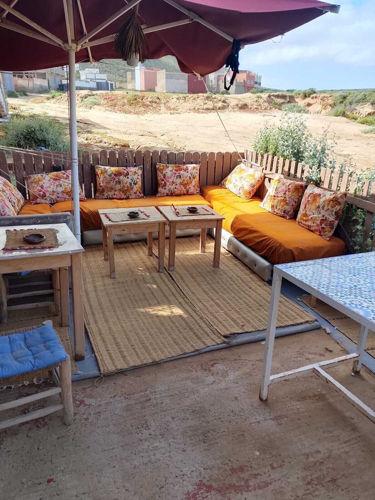 Un área de estar al aire libre con un banco de madera, dos mesas y una sombrilla grande.