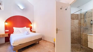 Una habitación de hotel con cama, pared de acento roja, zona de ducha y puerta blanca.