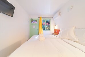 Una cama individual con ropa de cama blanca, una puerta verde con un ventanal y una cortina amarilla.