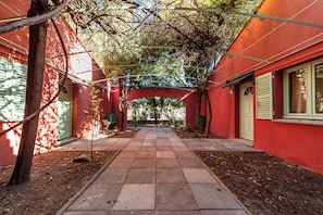 A pathway leading to a building with a red exterior and a covered area with trees. - Le Patio des Papes (Avignon)