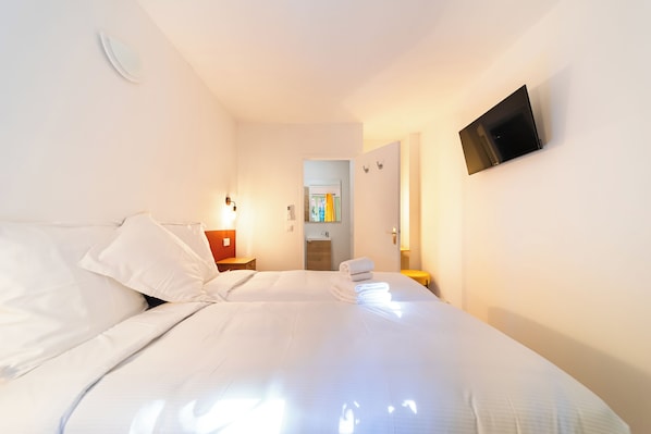 Quarto de hotel com cama, televisão na parede e banheiro visível através de uma porta aberta.