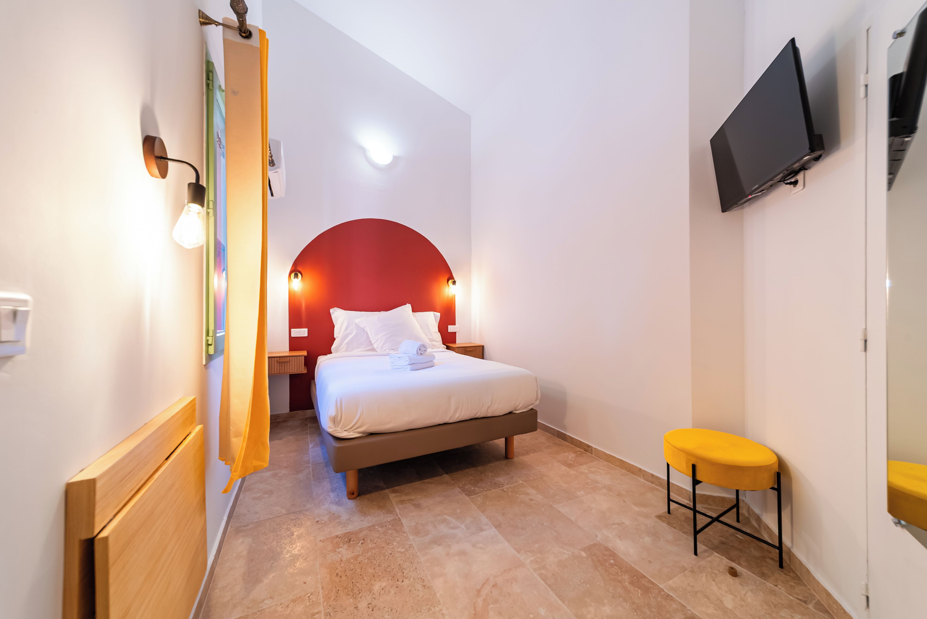 Habitación de hotel con cama, un taburete pequeño, un televisor y una pared de acento roja.