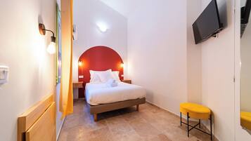 Habitación de hotel con cama, un taburete pequeño, un televisor y una pared de acento roja.