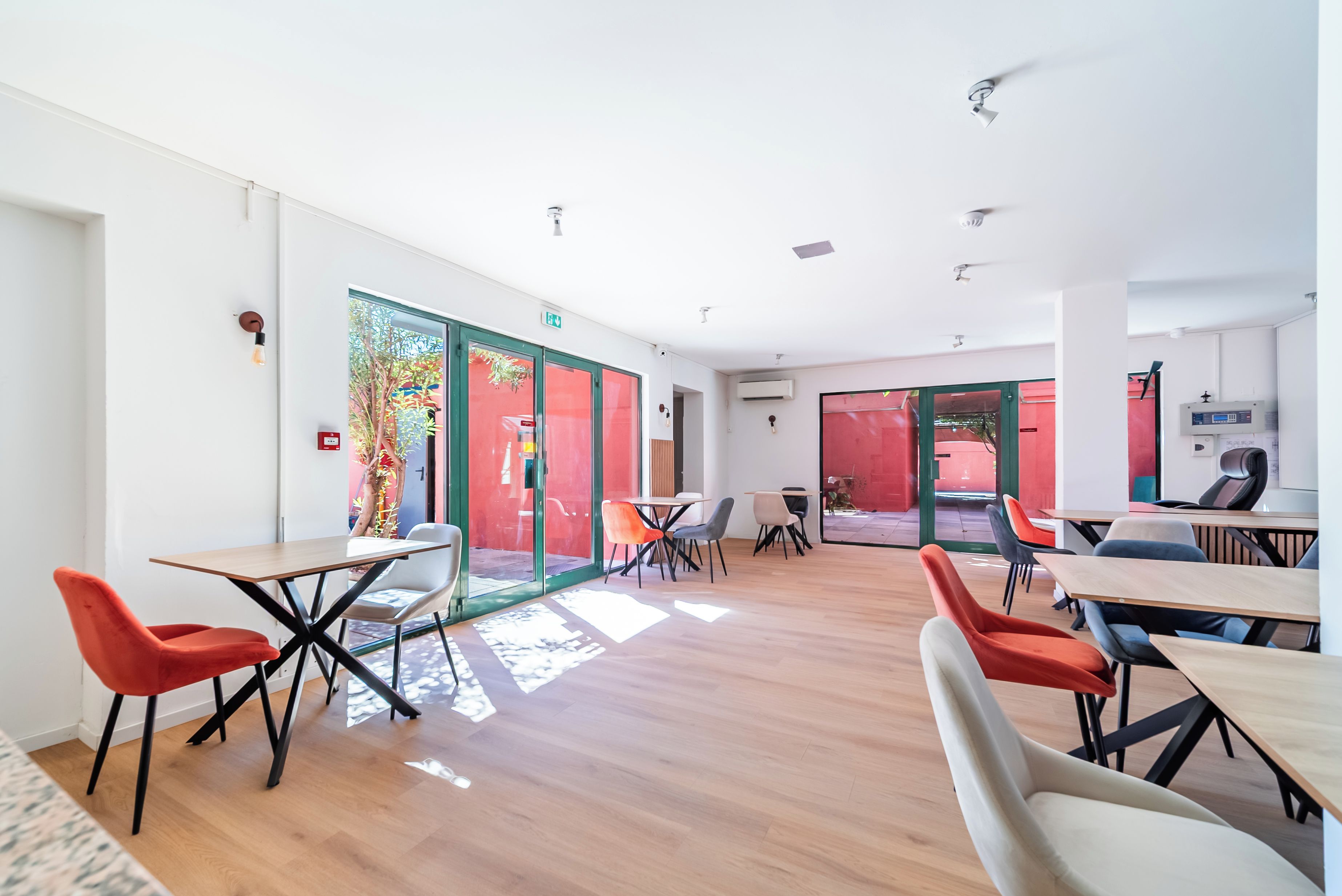 Un salón de conferencias moderno con puertas de cristal que dan a un espacio exterior, equipado con mesas y sillas.
