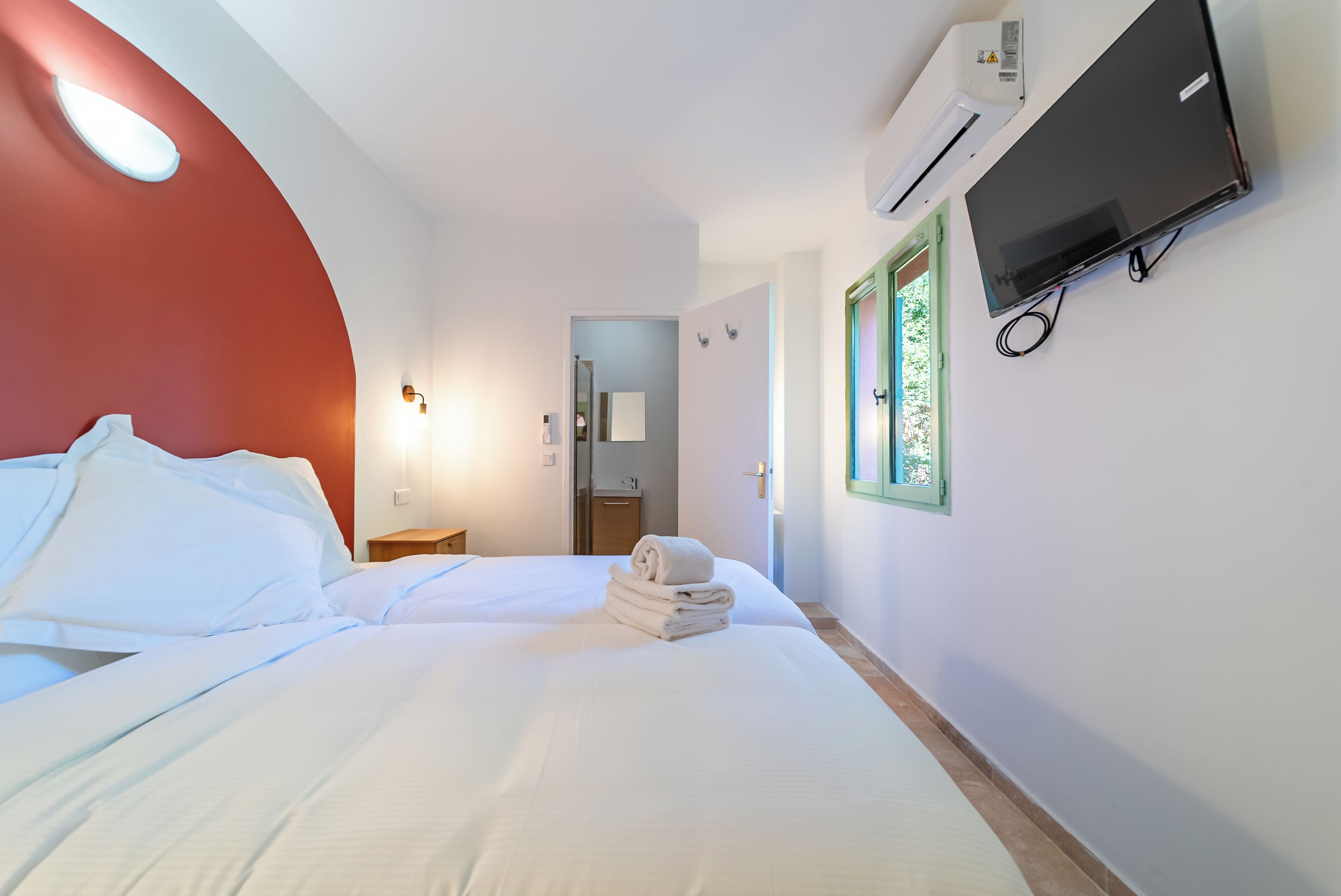 Habitación de hotel con una cama, un televisor montado en la pared, un equipo de aire acondicionado y una ventana con vistas.