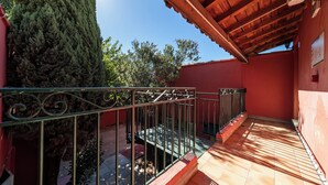 Un balcón con barandilla de metal, una planta en maceta y una pared roja.