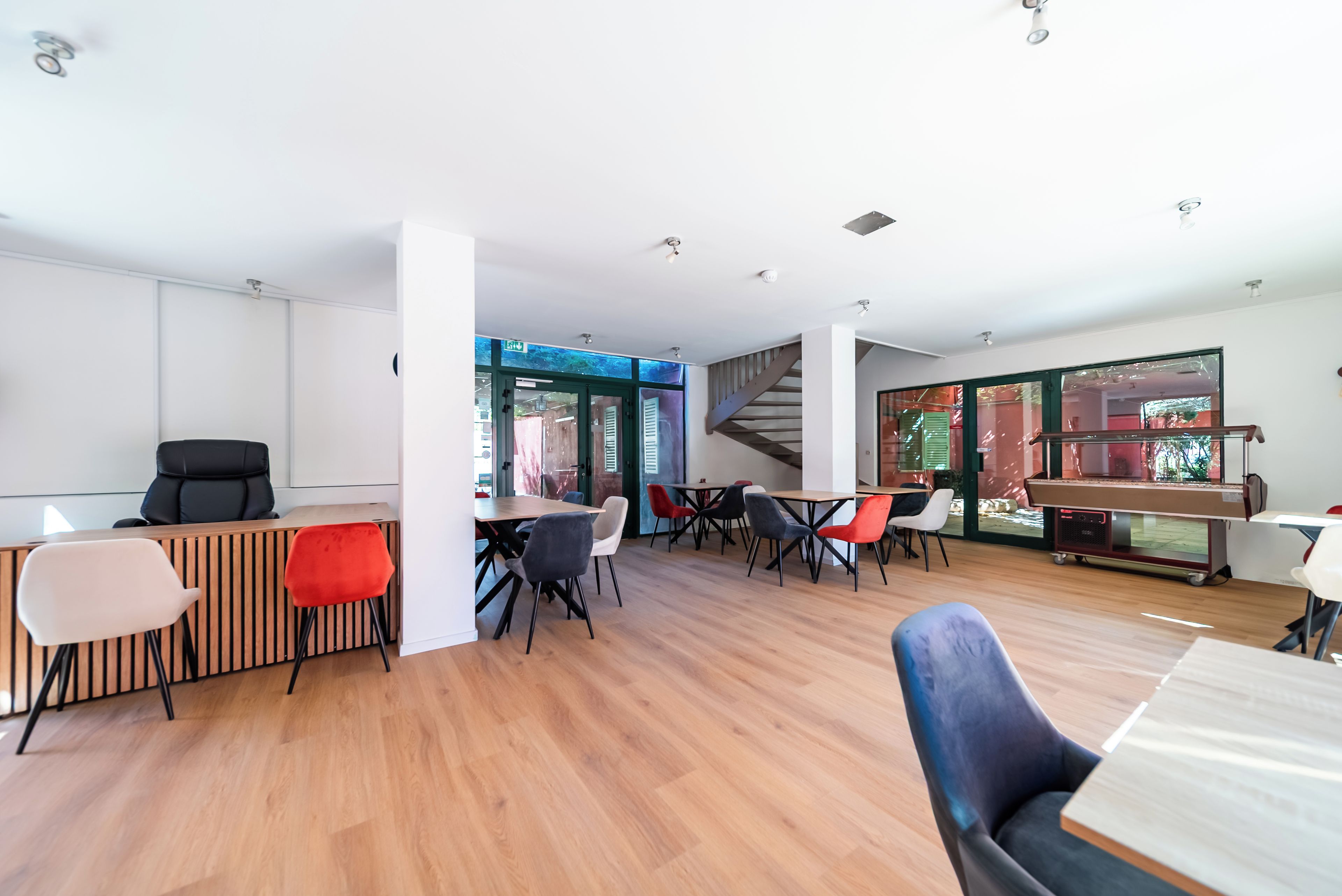 Un interior moderno con una recepción, varias áreas de estar y una escalera que sube a un nivel superior.