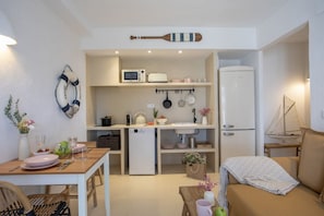 Eine kompakte Küche mit Mikrowelle, Wasserkocher und kleinem Kühlschrank. Im Wohnbereich befindet sich ein Esstisch mit Stühlen sowie eine Couch.