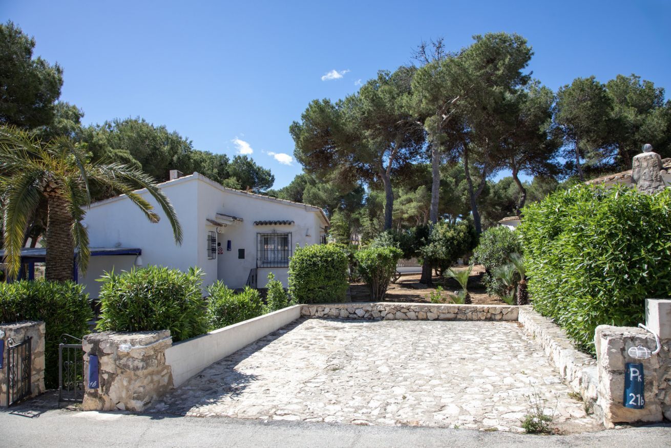 Un edifici blanc amb entrada d'adobes, envoltat de verdura i arbres.