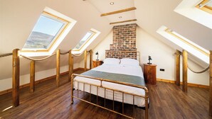 Ein Schlafzimmer mit schrägen Wänden, Oberlichtern, einem Kamin aus Backstein und einem Bettgestell aus Metall.