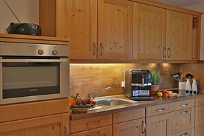 A kitchen with wooden cabinets, a built-in oven, a coffee maker, and a sink. - Rosemary - Sotterhof (Inzell)