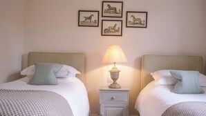 A double room with two beds, each with a pillow and a lamp on a nightstand between them. - Broomhill Cottage (Petworth)