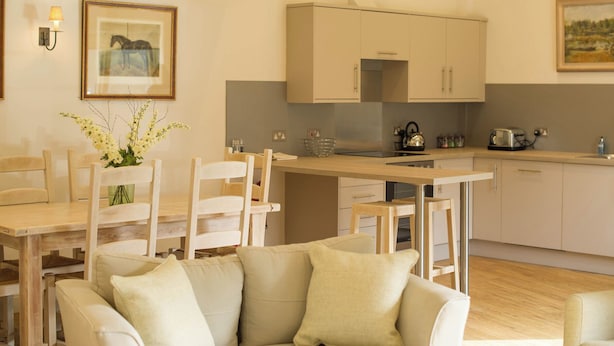 A modern kitchen with wooden cabinets, a dining table with chairs, and a sofa in a living area. - Broomhill Cottage (Petworth)