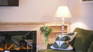 A living room with a green sofa, a fireplace, a table with a vase of flowers, and a lamp. - Broomhill Cottage (Petworth)