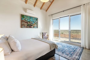 A bedroom with a large bed, a painting of famous landmarks, a window with a view of the desert, and a sliding glass door.