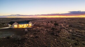 A modern house with a patio, surrounded by a dry, hilly landscape.
