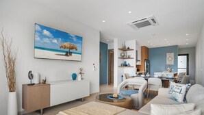 A modern living room with a beach-themed painting, a dining area with a kitchen in the background, and a cozy seating area. - Walishali 215 (Oranjestad)