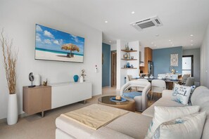 A modern living room with a beach-themed painting, a dining area with a kitchen in the background, and a cozy seating area. - Walishali 215 (Oranjestad)