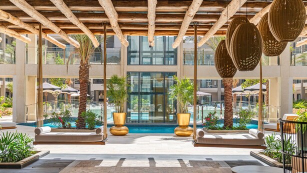 A pool area with palm trees, lounge chairs, and a modern building in the background. - Walishali 215 (Oranjestad)