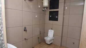 Pieni, laatoitettu kylpyhuone, jossa on wc, suihku ja pesuallas.