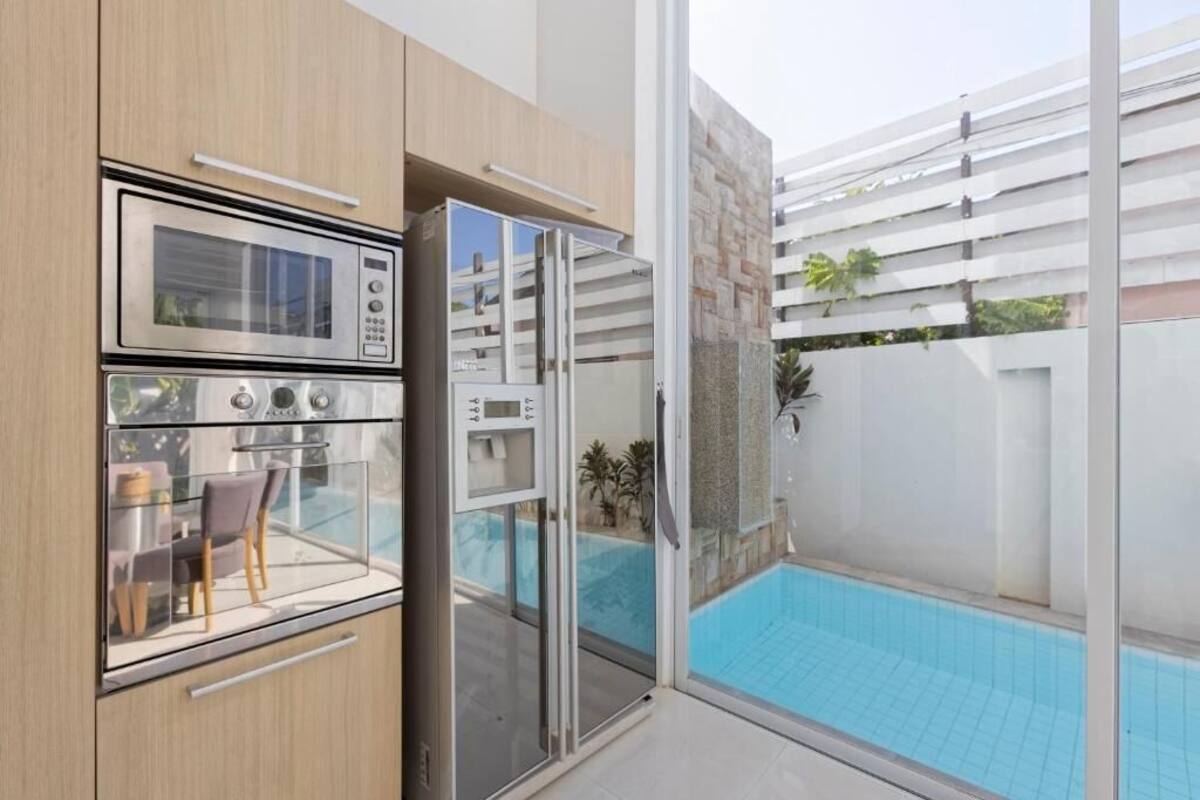 A modern kitchen with a built-in oven, a microwave, and a glass-enclosed dining area with a pool view.