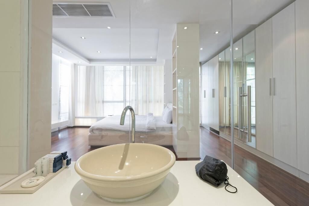 Un baño moderno con un lavamanos grande, un espejo y vistas a un dormitorio con cama y cortinas.