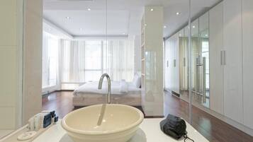 Un baño moderno con un lavamanos grande, un espejo y vistas a un dormitorio con cama y cortinas.