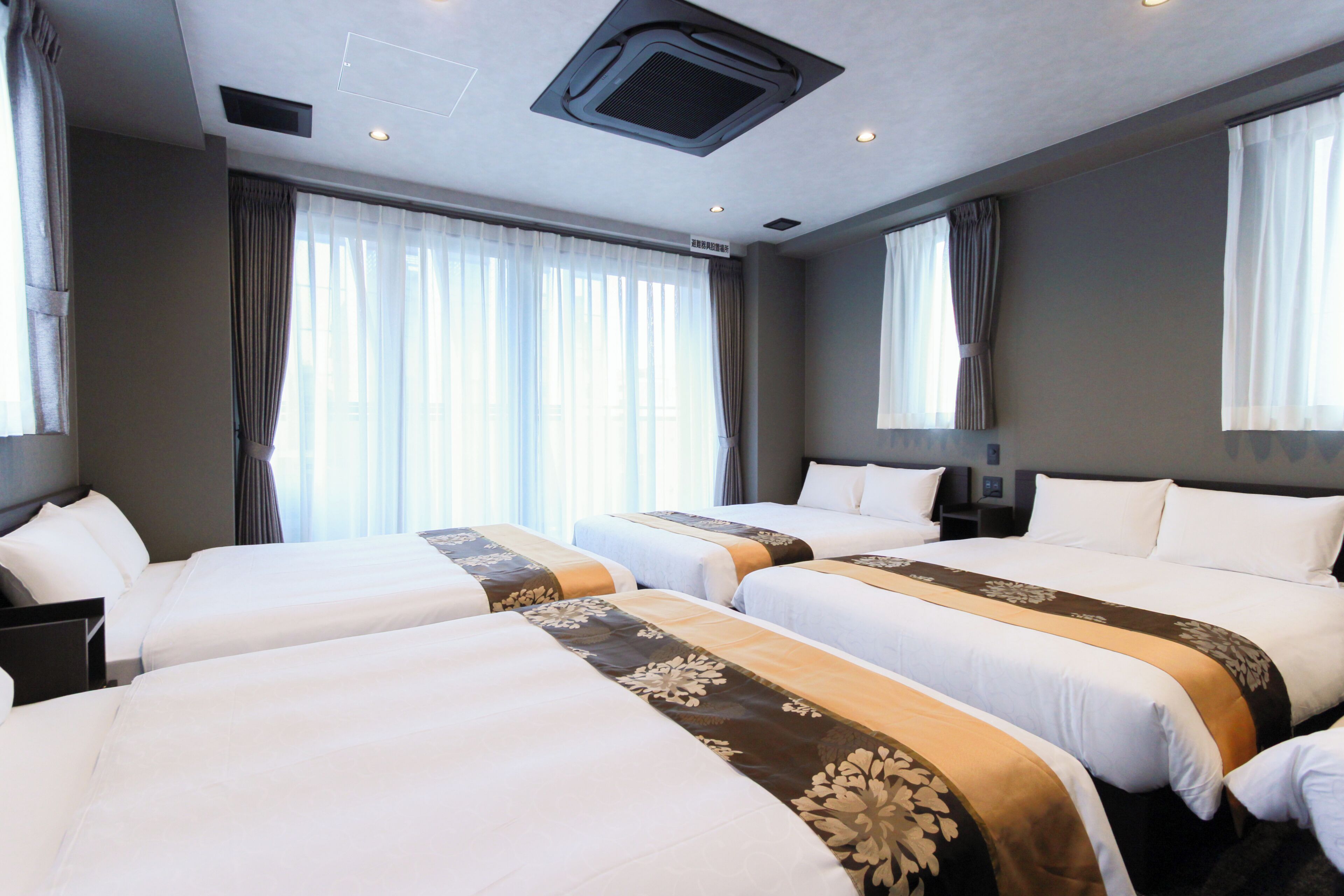 A hotel room with three beds, each with a patterned bedspread, a desk, and a chair.
