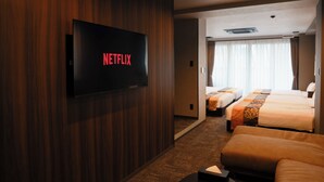 A hotel room with a large flat-screen TV displaying 'NETFLIX,' a bed, a sofa, and a corridor leading to another room. - OYADO LANTERN NAKASU KAWABATA (Fukuoka City)