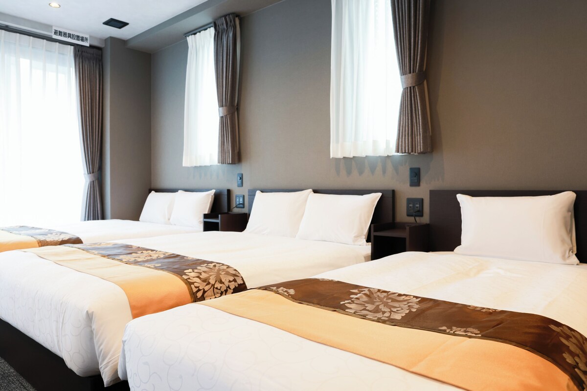 A hotel room with three beds, each with white bedding and brown floral accents.