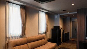 A modern hotel room with a sofa, a small table, a TV, and a kitchenette area. - OYADO LANTERN NAKASU KAWABATA (Fukuoka City)