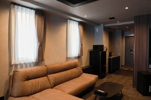A modern hotel room with a sofa, a small table, a TV, and a kitchenette area. - OYADO LANTERN NAKASU KAWABATA (Fukuoka City)