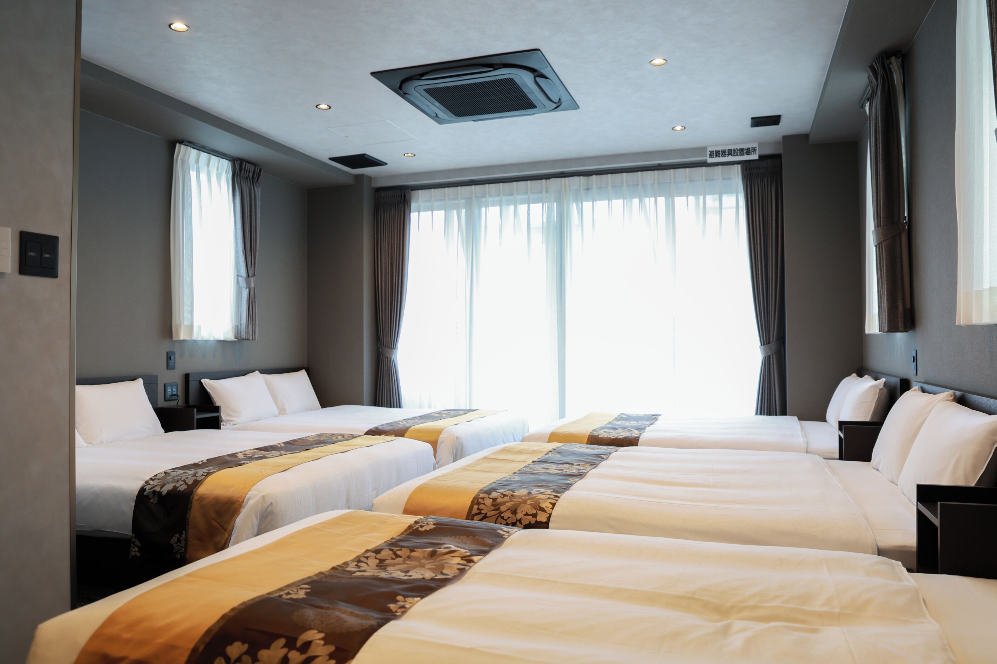 A hotel room with two beds, a ceiling vent, and a large window with curtains.