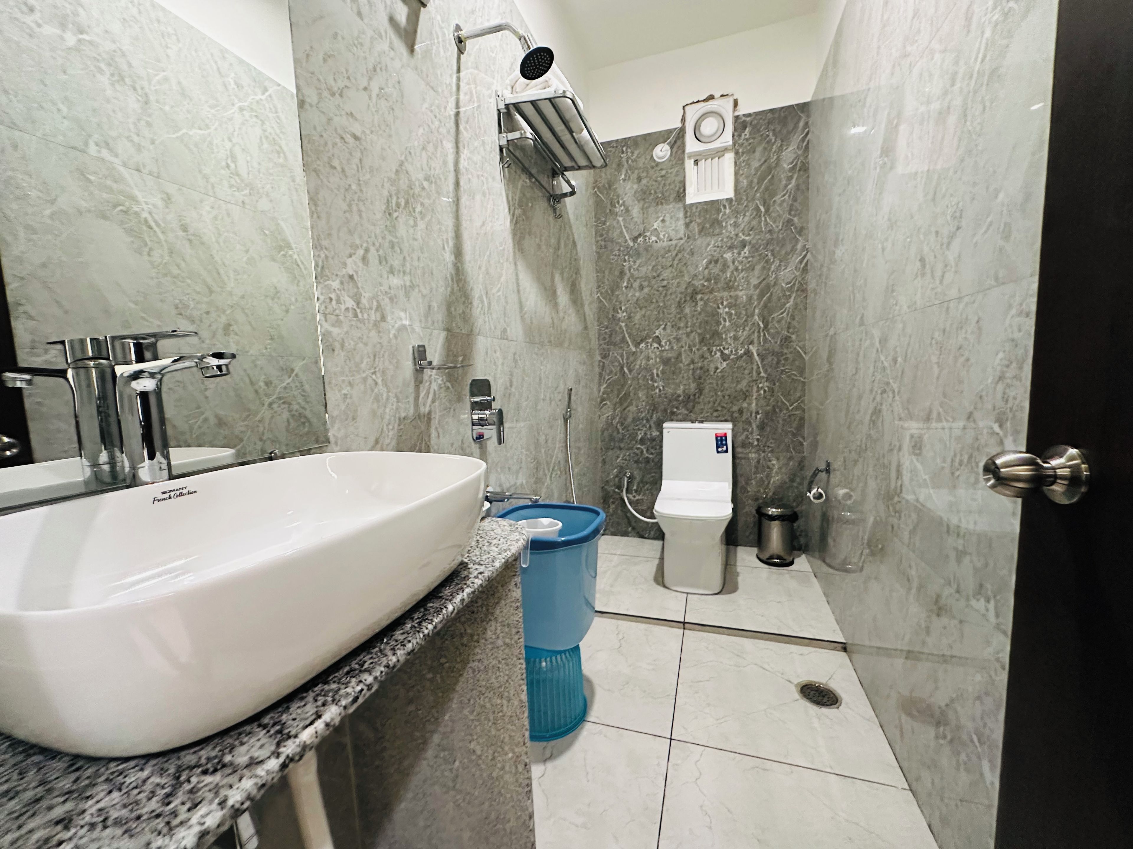 Une salle de bain avec un grand lavabo blanc, une pomme de douche, des toilettes et une poubelle.