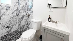 A bathroom with a toilet, sink, mirror, and shower with marble tiles.