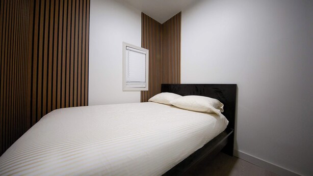 A bedroom with a bed, a window, and a wall with vertical wooden slats. - 3bdrm Apt next to Airport/Downtown 7 min drive (Chelsea)