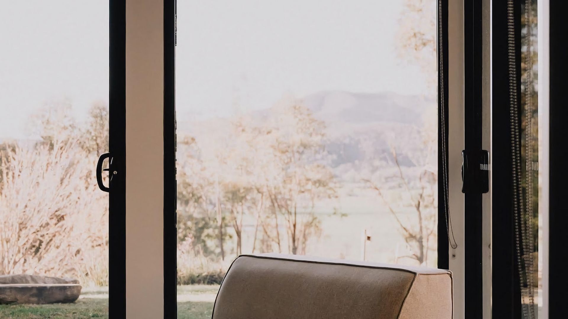 A room with a view of a lake and trees, a door with a handle, and a chair.