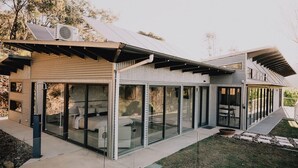 Ein modernes Haus mit einer verglasten Terrasse, einem überdachten Außenbereich und einer Solarpanel-Anlage.
