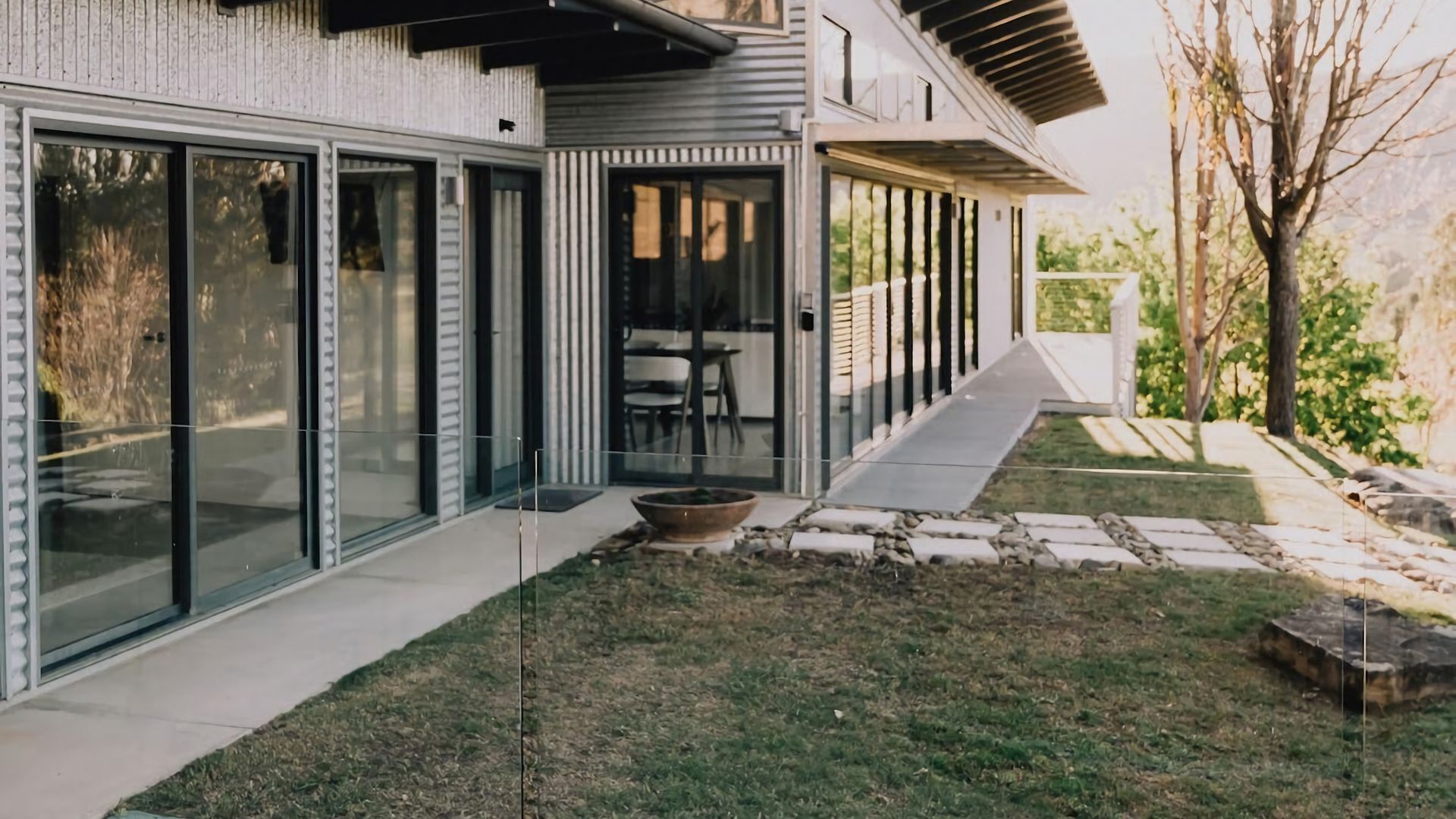 A modern house with large glass doors, a stone pathway, and a small garden area.