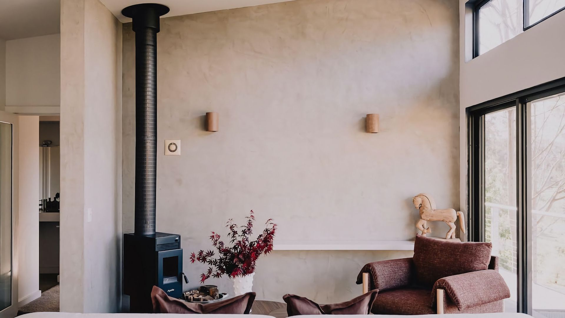A modern living room with a fireplace, a vase of red flowers, and a wooden horse sculpture.
