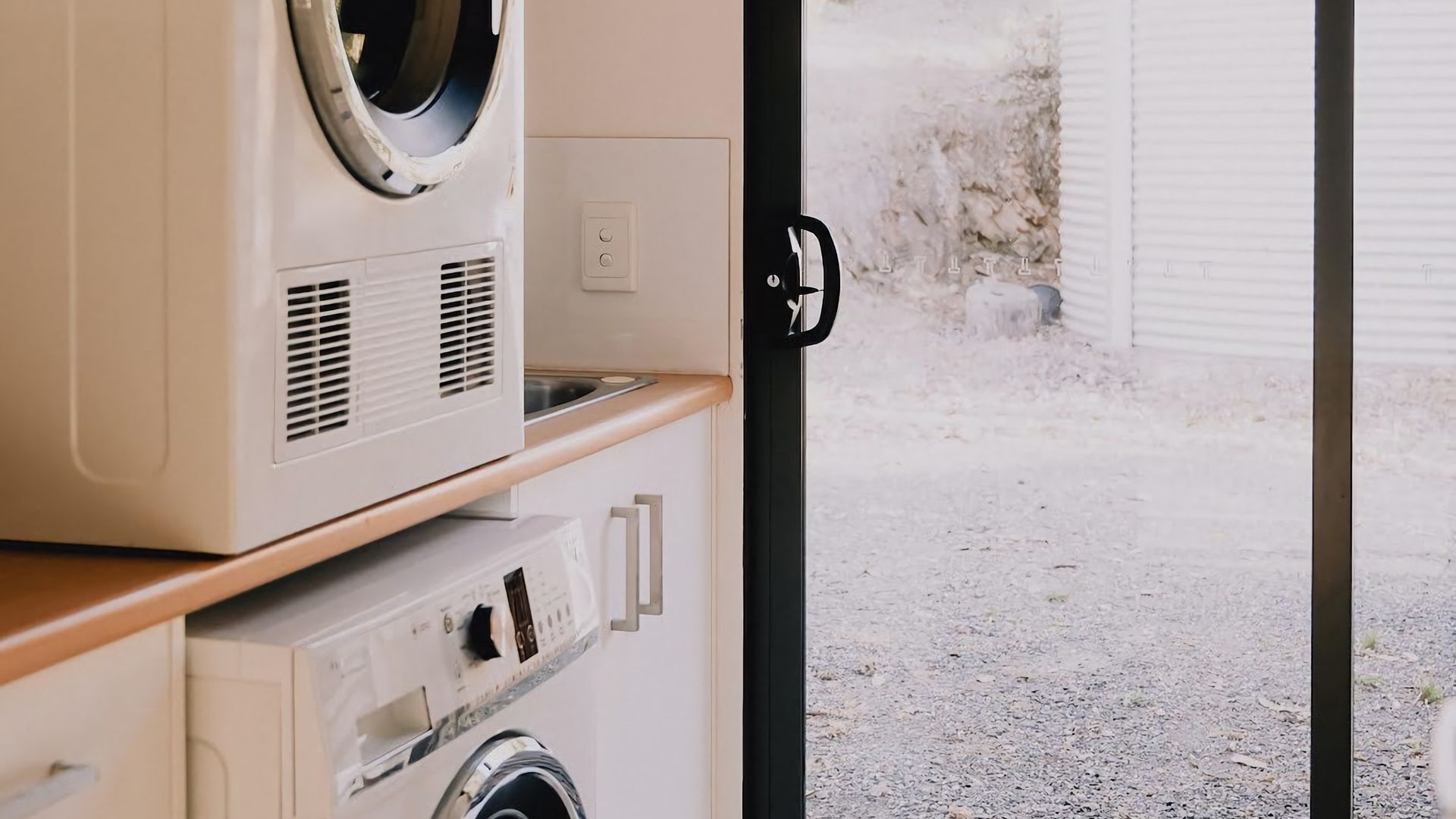 A laundry room with a washing machine and dryer, a wooden counter, and a door leading outside.