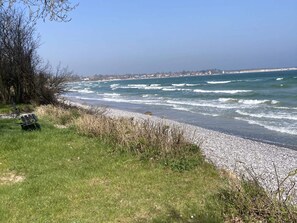 A coastal view with a pebble beach, a bench, and a grassy area. - 4 Star Holiday Home in Rodvig Stevns (Rodvig Stevns)