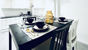Une cuisine moderne avec des meubles blancs, une table à manger dressée avec des bols noirs, un vase doré et une machine à café.