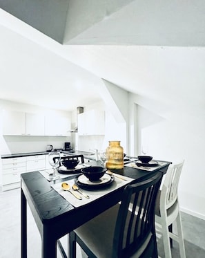 A modern kitchen with white cabinets, a dining table set with black bowls, a golden vase, and a coffee machine. - Spacious 5BR Apartment Near Liesing (Wien)