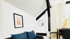 Un salon moderne avec un canapé gris, une table basse noire, un tableau encadré, un miroir rond et une petite table ornée de fleurs.