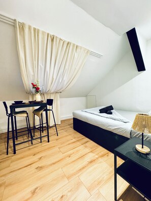 Ein modernes Zimmer mit Schlafplatz in der Schlafloge, einem Esstisch mit Stühlen und einem kleinen Nachttisch mit Lampe.