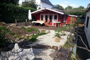 Ein rotes Haus mit Terrasse, kleinem Garten und einem Kiesweg.