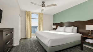 Ein Hotelzimmer mit einem Bett, einem Schreibtisch, einem Schminktisch, einem Deckenventilator und einem Fenster mit Vorhängen.
