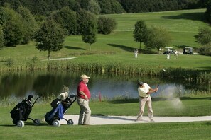 Ein Golfplatz mit Teich, Bäumen und einem Wanderweg.
