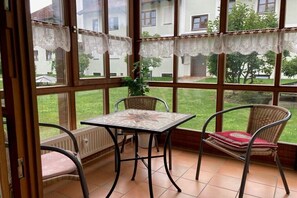 Ein Zimmer mit Tisch, Stühlen, großen Fenstern und Blick auf ein Gebäude sowie Grünflächen.